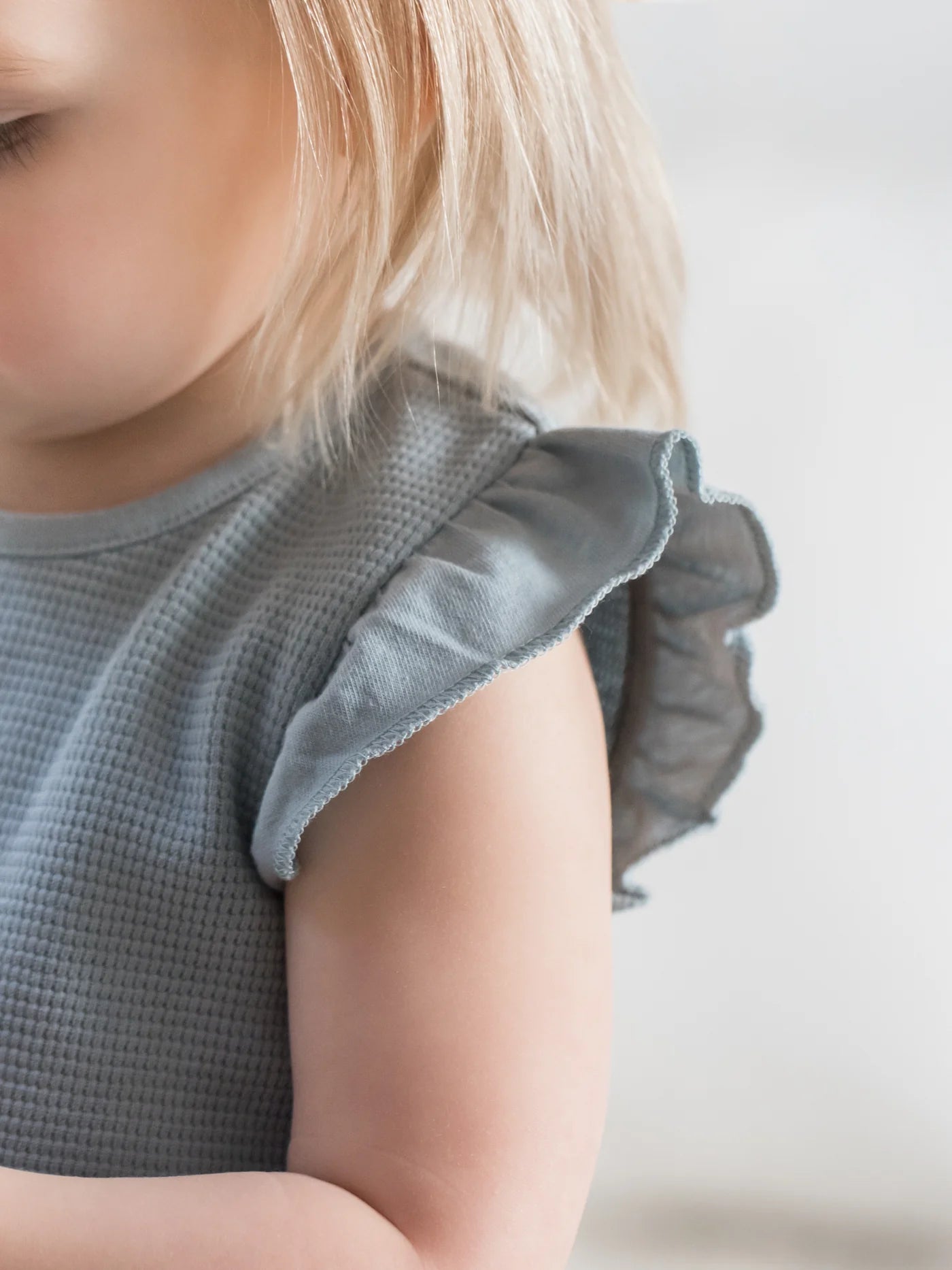 Our Maci Flutter Tank Romper is made from 100% organic waffled cotton, with eco-friendly coconut buttons and nickel-free snaps. The adorable flutter sleeve and neckl