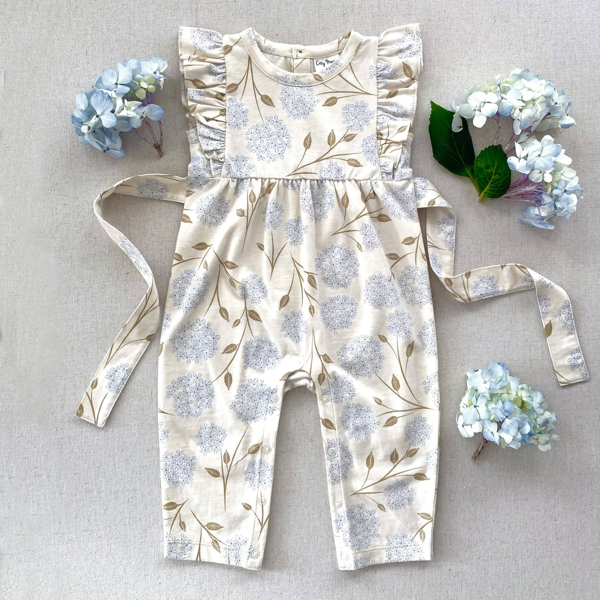Made with the softest 100% combed cotton jersey. Featuring coconut buttons on back, a wrap around tie, and flutters on the shoulders. In our all over Hydrangea print